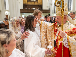 A bishop in ornate robes blesses a woman holding a candle in a church ceremony. People watch nearby, creating a solemn atmosphere.