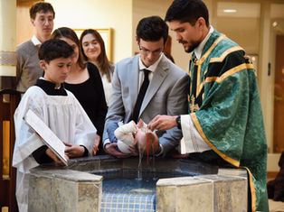 Priest baptizes a baby at a stone font while family and altar boys watch in a church, solemn and warm-lit.