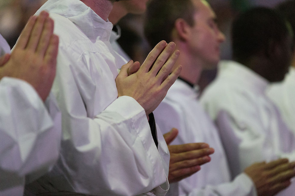 People in white robes stand with hands clasped in prayer. The setting is a solemn indoor gathering with soft lighting, creating a serene mood.