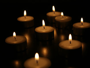 Lit tealight candles arranged in a dark setting, casting warm, soft glows and reflections on a smooth surface, creating a calming mood.