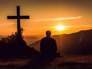 Silhouette of person sitting near a cross, gazing at a vibrant orange sunset over hills, creating a serene and contemplative mood.