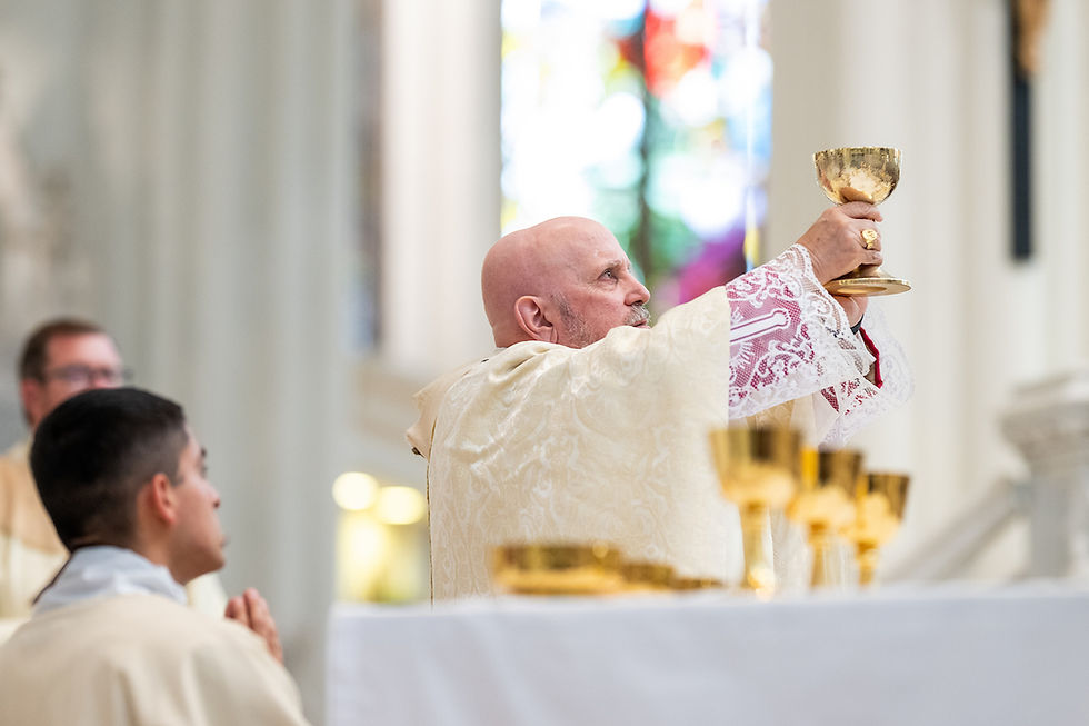 Bishop in ornate robes holds up a gold chalice during a church ceremony, with stained glass in the background. Solemn atmosphere.