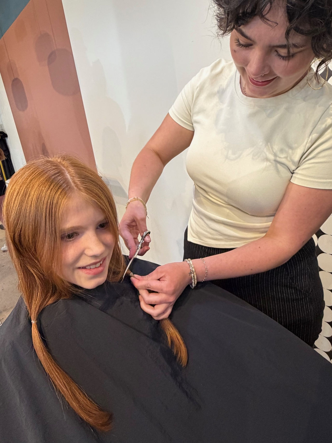 Close-up of a stylist cutting one of two braided sections of a girl’s red hair.