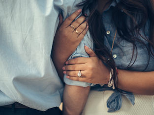 Close-up of two people in blue shirts with entwined arms, focusing on hands adorned with rings, conveying intimacy and connection.