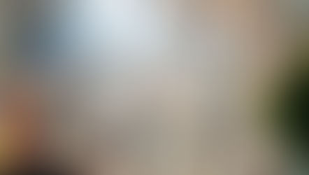 Priests in white robes sit in a cathedral with stained glass windows. Sunlight streams in, creating a serene atmosphere.