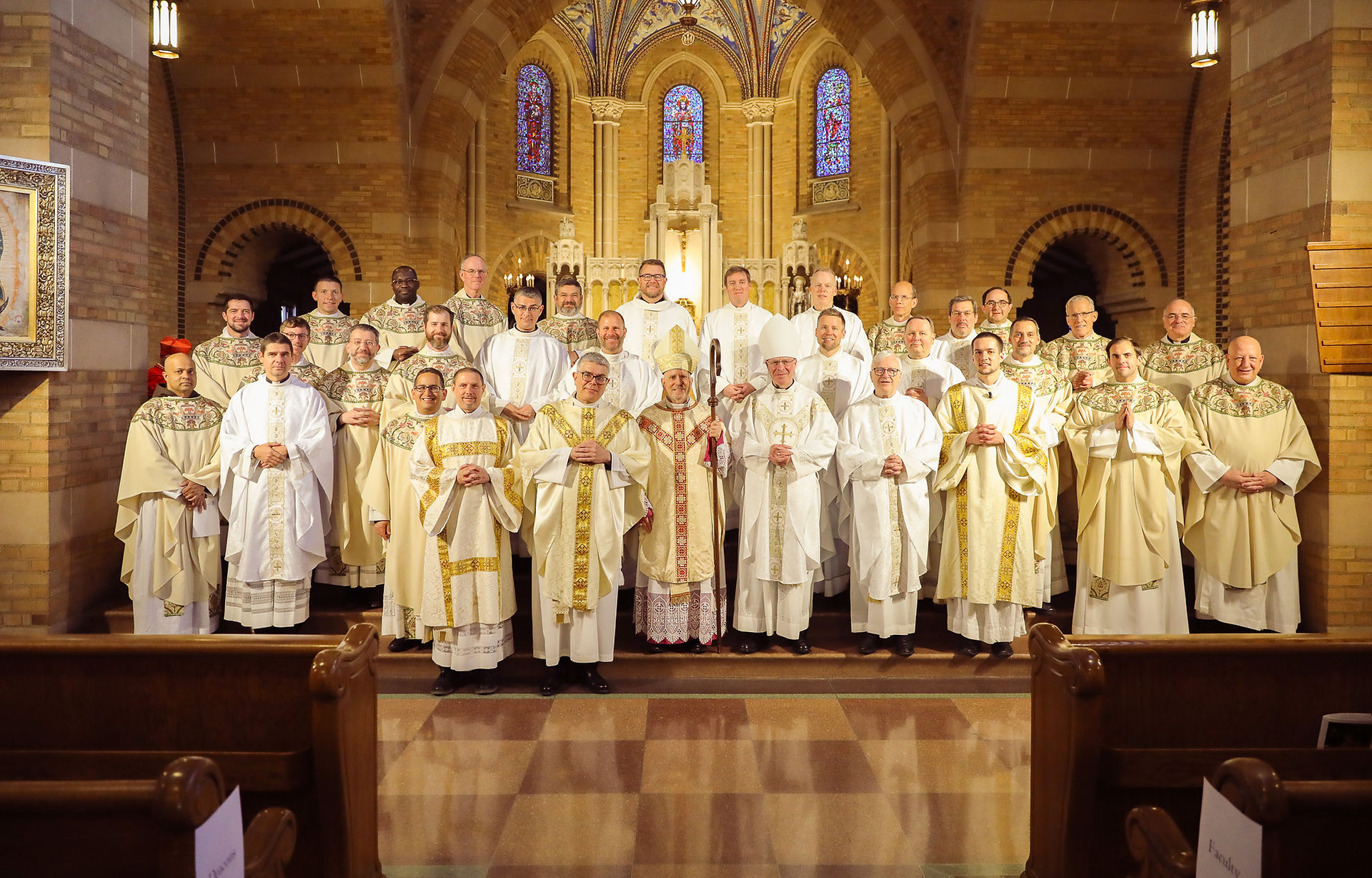 Priests, deacons and bishops stand for a photo in an ornate brick chapel following a religious ceremony.