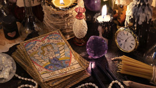 Tarot card "The Lovers" amid candles, clock, and crystals on a mystical table. Warm glow and vintage objects create an enchanting setting.