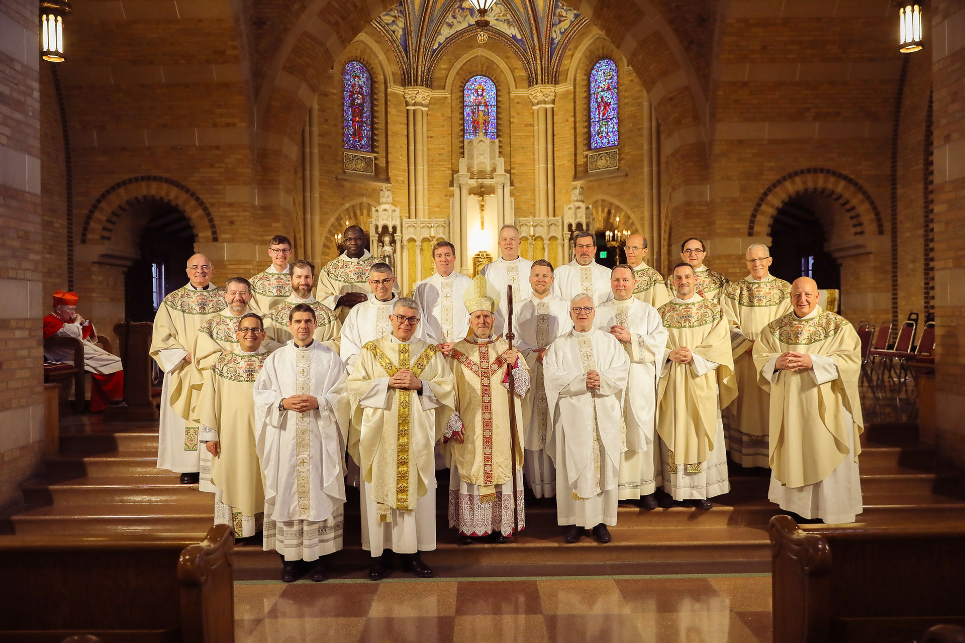 Priests, deacons and bishops stand for a photo in an ornate brick chapel following a religious ceremony.