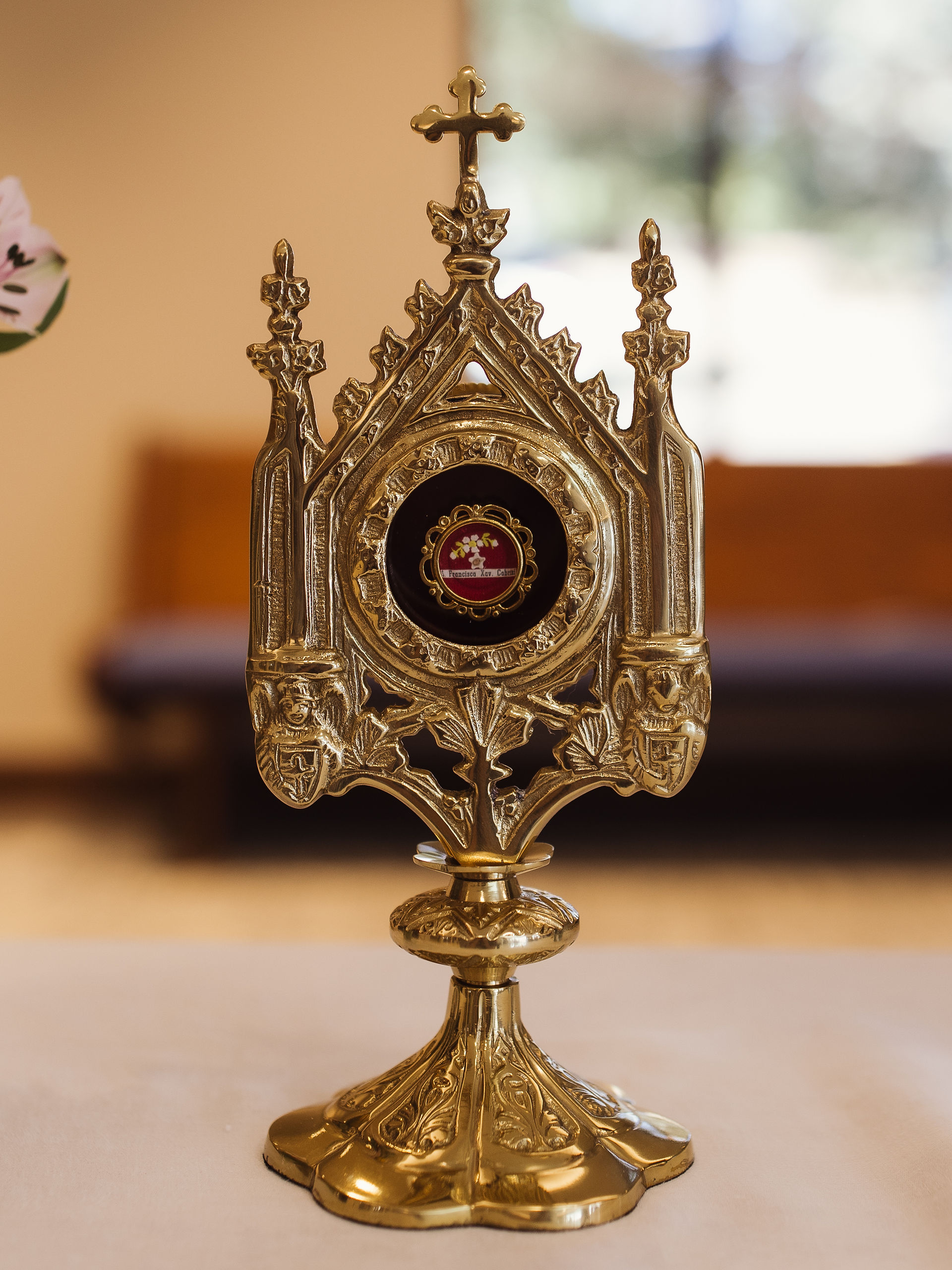 Ornate gold reliquary on a table, featuring intricate details and a central relic of St. Frances Xavier Cabrini. Background is softly blurred, creating a serene mood.