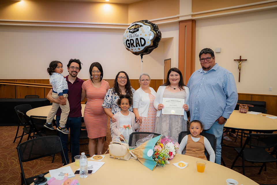 Family celebrates a graduate in a church hall, holding a certificate under a Congrats to the Grad balloon.