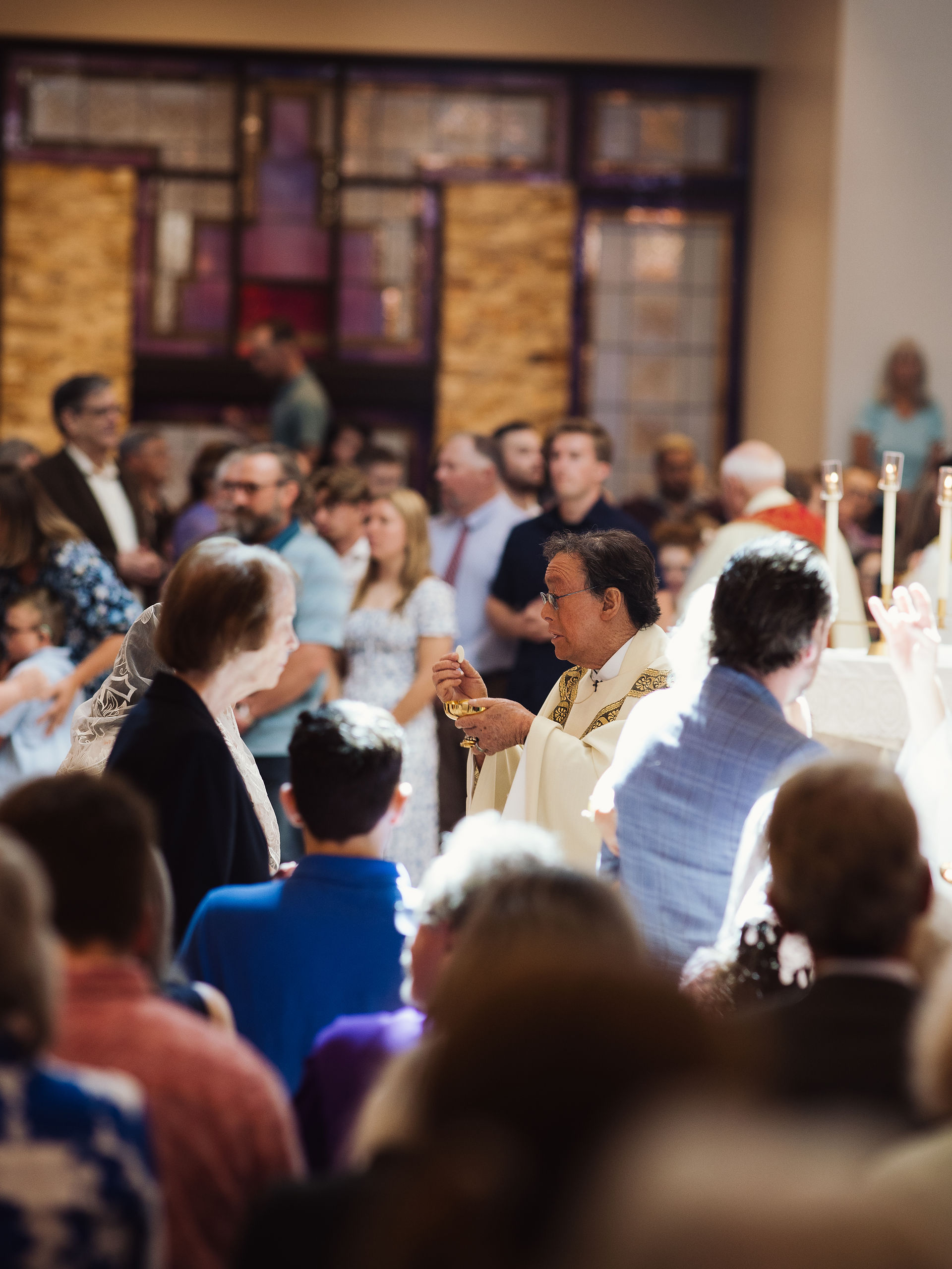 Priest giving communion to a woman in a church, with a congregation in the background. The mood is reverent, with warm lighting.