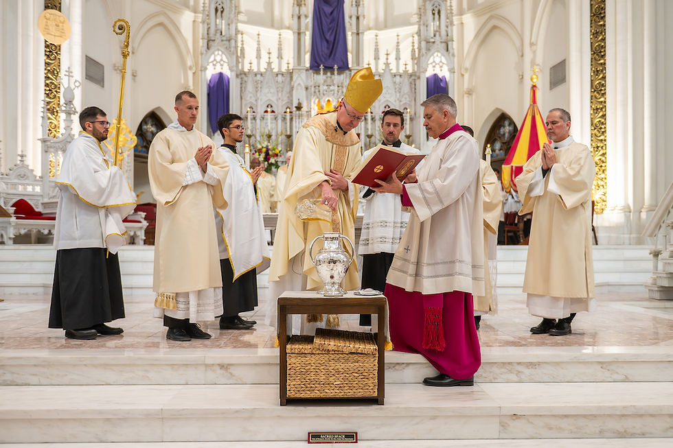 Clergy in white and gold robes conduct a religious ceremony in a grand cathedral. One holds a book, another pours oil. The mood is solemn.