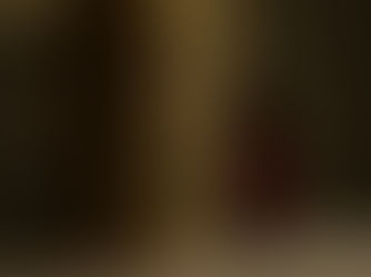 Golden tabernacle with engraved cross beside a glowing red candle in a dimly lit setting, creating a serene and reverent atmosphere.