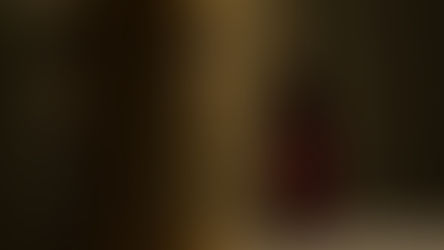 Golden tabernacle with engraved cross beside a glowing red candle in a dimly lit setting, creating a serene and reverent atmosphere.