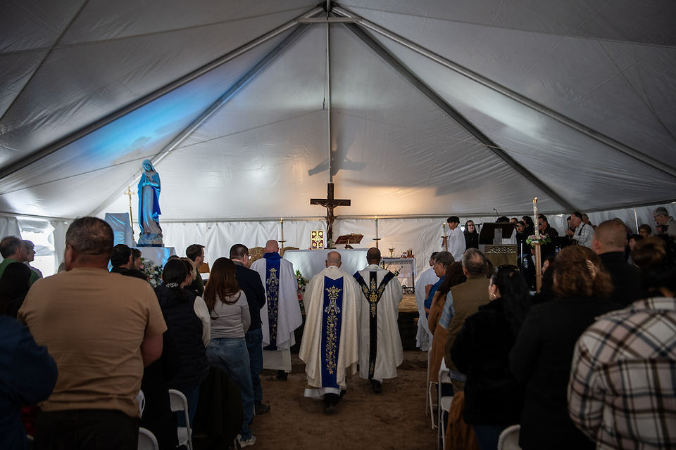 Priests process toward an altar during Mass celebrated inside a large white tent filled with parishioners.