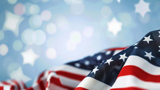 Folded American flag with stars and red-white stripes against a soft blue background with glowing star shapes