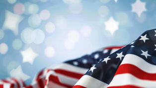 Folded American flag with stars and red-white stripes against a soft blue background with glowing star shapes