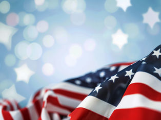 Folded American flag with stars and red-white stripes against a soft blue background with glowing star shapes
