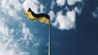 Ukrainian flag waving on a flagpole against a bright blue sky with scattered white clouds, conveying a sense of freedom and openness.