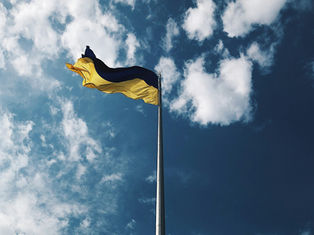 Ukrainian flag waving on a flagpole against a bright blue sky with scattered white clouds, conveying a sense of freedom and openness.