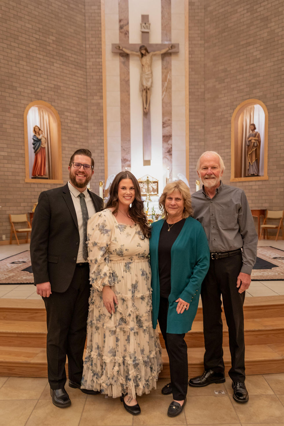 Four people smiling inside a church, standing in front of an altar with a crucifix. The setting is warm and peaceful.