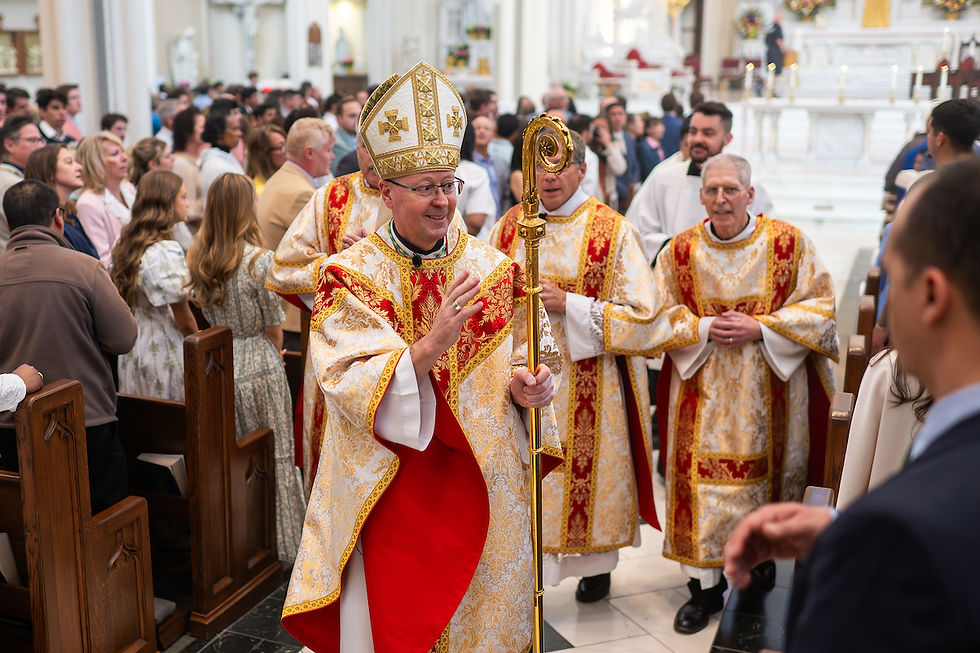 A bishop in ornate robes and mitre holds a staff, leading a procession in a crowded church. Attendees watch attentively.
