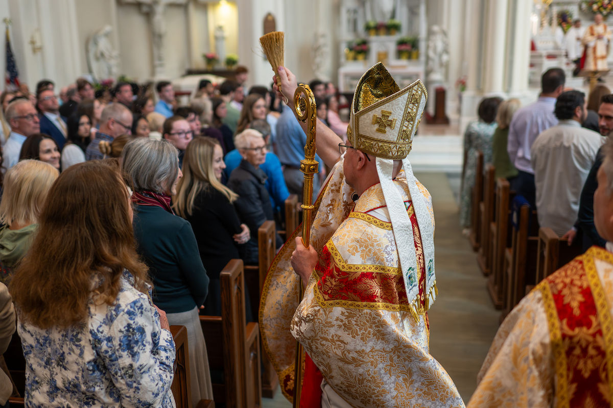 A bishop sprinkles holy water on the congregation while walking down the aisle during Mass.