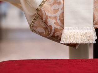 Elegant ivory and gold-patterned fabric with fringe detail hangs over a red textured surface, creating a refined, serene atmosphere.