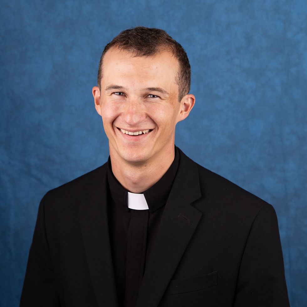 Smiling young priest in a black suit and clerical collar against a blue studio backdrop
