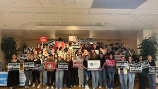 A group of people holds pro-life signs in an indoor setting. The mood is organized and unified, with visible text supporting their cause.