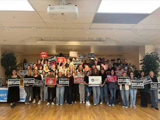 A group of people holds pro-life signs in an indoor setting. The mood is organized and unified, with visible text supporting their cause.