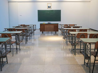Empty classroom with rows of desks facing a green chalkboard, teacher's desk, and wall map in bright light.
