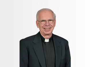 Smiling man in clerical attire with a white collar and glasses, set against a plain white background.