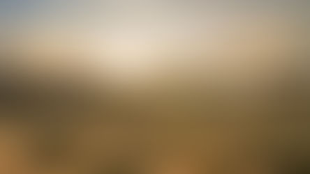Sunset over a desert landscape with sparse bushes, distant mountains, and a vapor trail in the sky, creating a warm, tranquil scene.