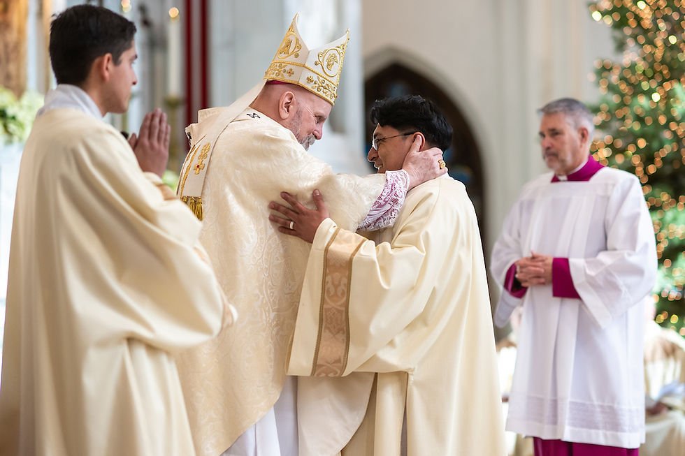 A bishop in ornate robes hugs a priest warmly in a church. Two other clergymen watch. Background shows soft lights, creating a serene mood.