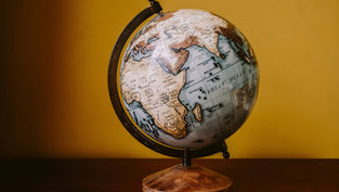 A globe on a wooden table against a yellow wall, showing Africa and the Indian Ocean. The image has a warm, nostalgic feel.