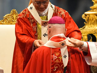 Two Catholic clerics in ornate red vestments during a solemn ceremony, one placing a stole on the other before a gold altar.