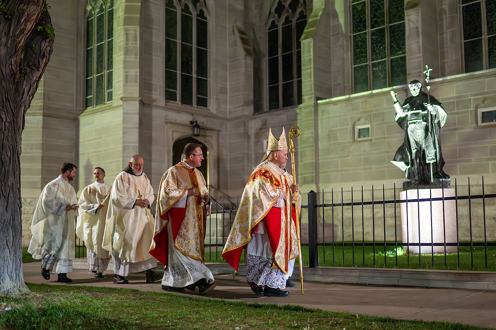 Clergy in ornate robes walk outside a lit cathedral at night, passing a statue. The mood is solemn and ceremonial.