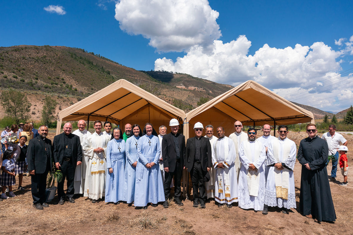 Group of clergy and religious leaders posing outdoors under beige tents in a mountain valley on a bright sunny day
