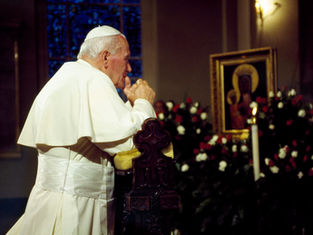 Man in white robe praying at a church altar, hands clasped. Icon and flowers in background, warm lighting, contemplative mood.