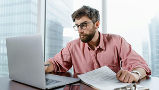 A businessman hunches over his computer, looking stressed, as he works on a project.