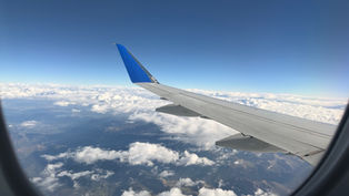 Airplane wing seen from a window above white clouds and mountains under a clear blue sky, calm and expansive view