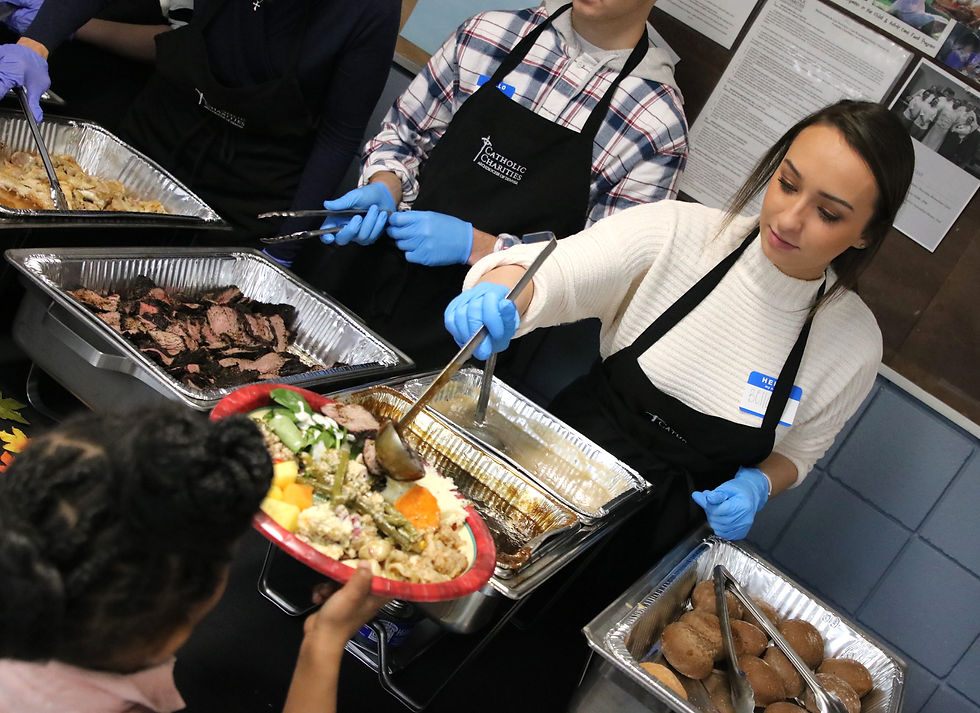 Volunteers in aprons serve food from trays to a child holding a plate. They wear blue gloves, and a sense of community is evident.