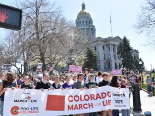 Crowd holds "Colorado March for Life" banner outside the Colorado State Capitol. Participants carry signs, showing a peaceful protest.