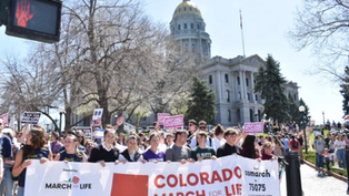 Crowd holds "Colorado March for Life" banner outside the Colorado State Capitol. Participants carry signs, showing a peaceful protest.