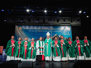 Catholic clergy in green vestments pose on stage before a banner for the National Conference of Burmese-American Catholics.