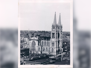 Aerial view of a large Gothic cathedral with twin spires, surrounded by trees and buildings. Black and white image with a calm atmosphere.