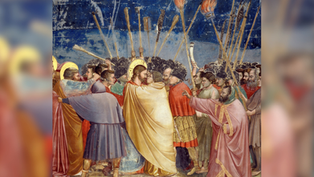 A dramatic scene with a group of people holding torches. A man in a golden robe is embraced. The night sky is in the background.