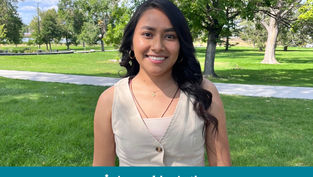 Smiling woman in a cream top stands in a sunny park with green grass and trees. Blue banner at bottom reads "Appeal in Action."