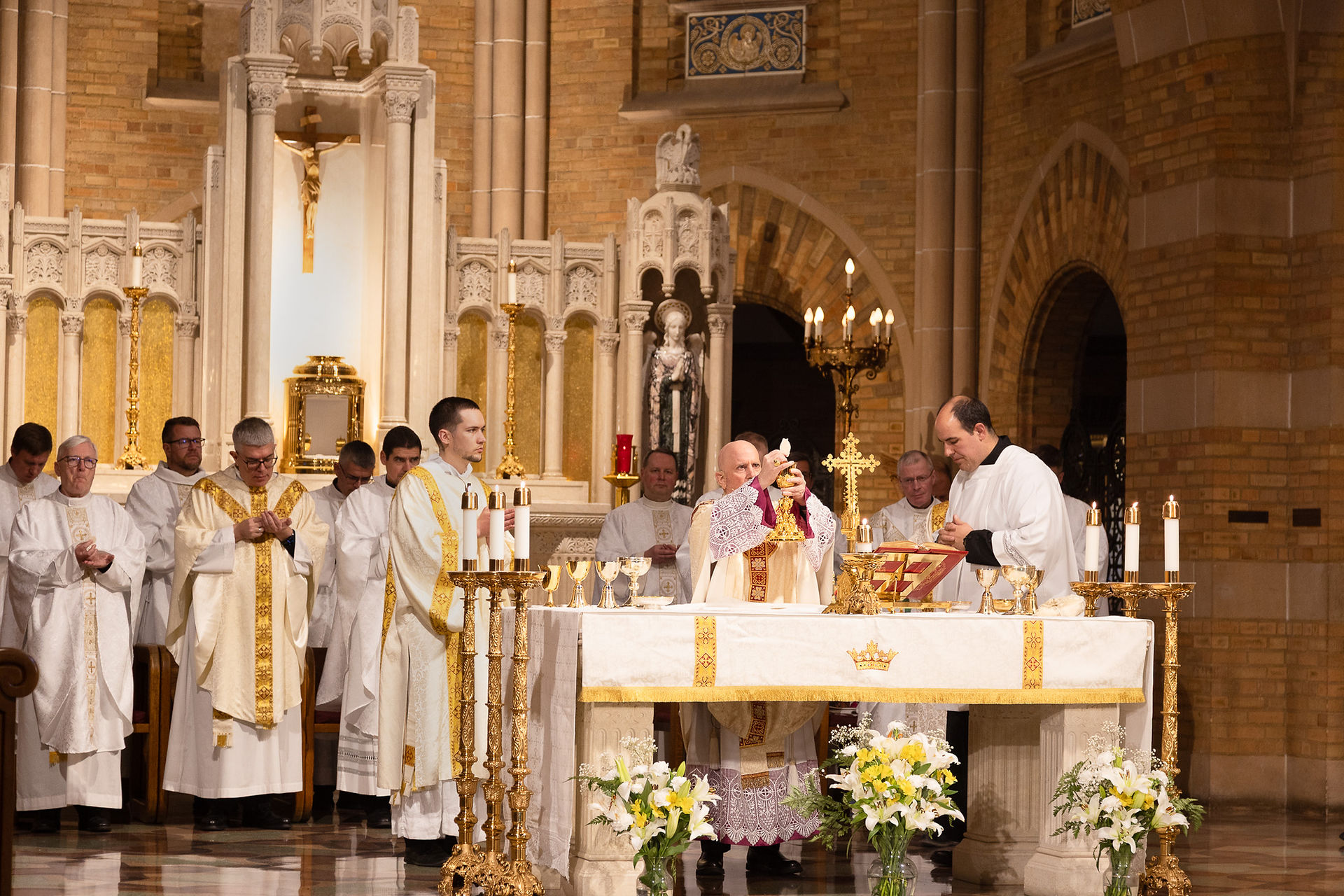 An archbishop celebrates Mass surrounded by other priests and deacons in a beautiful, ornate chapel.